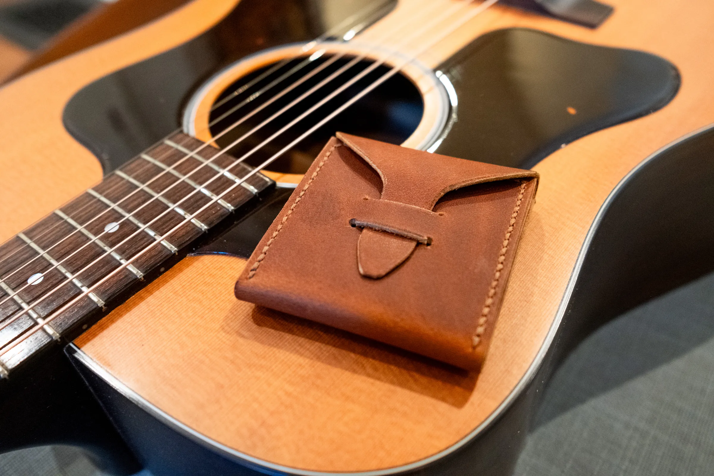 A closed brown pick case resting on the top of an acoustic guitar